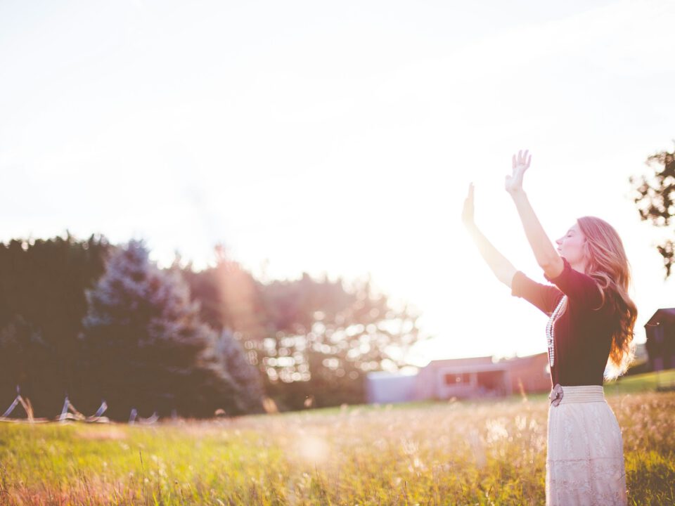 Frau steht in einer sonnendurchfluteten Wiese mit erhobenen Armen – symbolisch für Freiheit, spirituelles Wachstum und Energiearbeit im astrologischen Coaching.